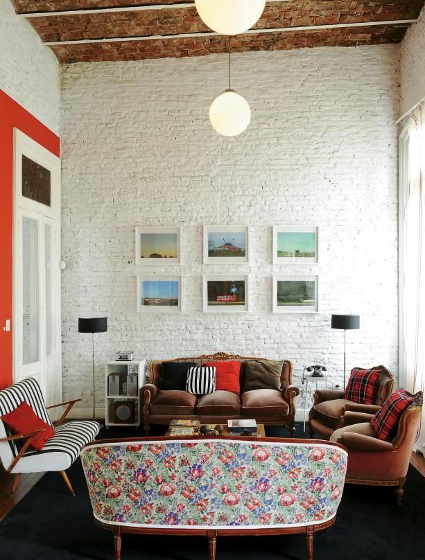 A mid century modern living room with whitewashed brick walls, elegant sofas and chairs, a chic gallery wall, bright and printed pillows and pendant lamps