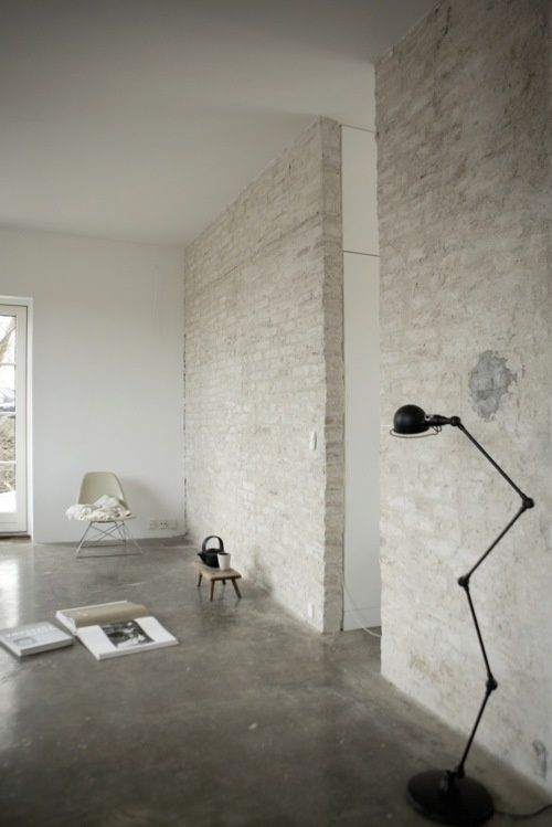 a Nordic space with whitewashed brick walls and a concrete floor, a black floor lamp and some furniture