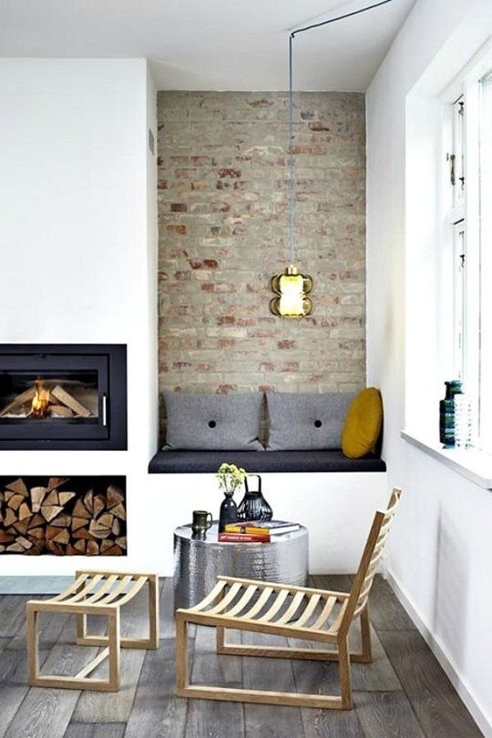 A Scandinavian space with a built in fireplace and firewood storage, an upholstered built in bench with pillows is a welcoming and cool nook