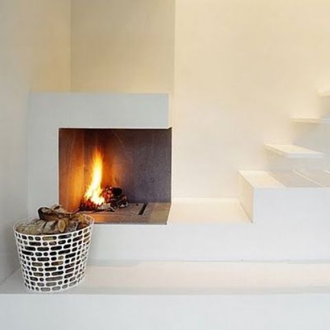 a minimalist nook with an open fireplace by the staircase and a metal basket for firewood plus a small nook to sit on the steps