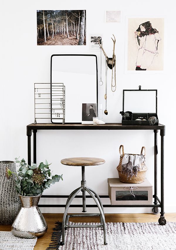 a small and pretty industrial working space with a metal console table, a metal and wood stool, various jewelry on stands and some decor