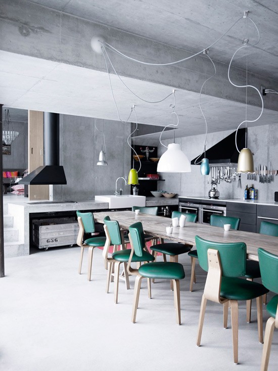 Bare concrete walls and ceilings is one of those things you can often find in industrial kitchens. On this kitchen creative light fixture and emerald chairs add a color splash concrete need.