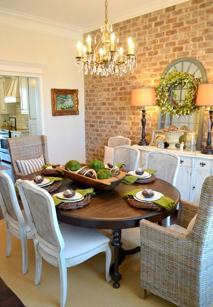 A vintage rustic dining space with an exposed brick accent wall, a vintage white sideboard, a dark stained dining table, chic upholstered and wicker chairs in neutrals and a vintage crystal chandelier