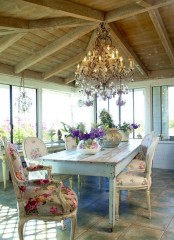 a refined vintage meets shabby chic dining room with a shabby chic table and floral chairs, an oversized crystal chandelier and lots of bright blooms on the table