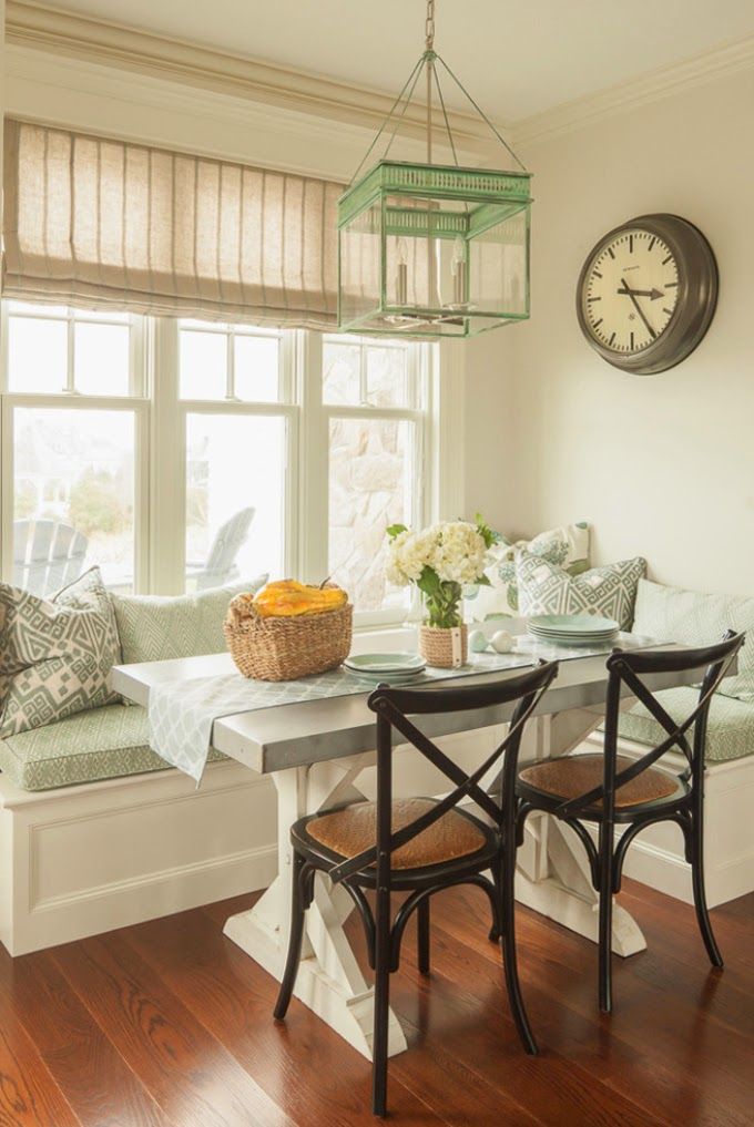 A vintage rustic dining space with a windowsill seat with pillows, a neutral dining table, dark stained dining chairs and a catchy mint pendant lamp