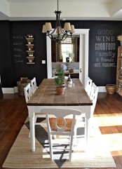 a vintage rustic dining space with chalkboard walls, a dining table with a stained tabletop, white chairs and a vintage chandelier over the table