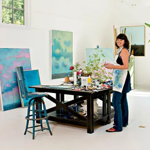 a white home artist studio with a black table, a small stool and lots of bright artwork and paints around is amazing for painting