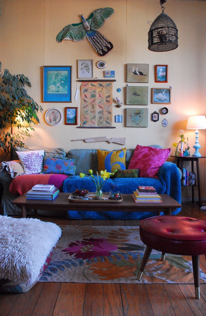 In this colorful living space, the use of vertical spacefrom wall art to a hanging bird cage is quite interesting .