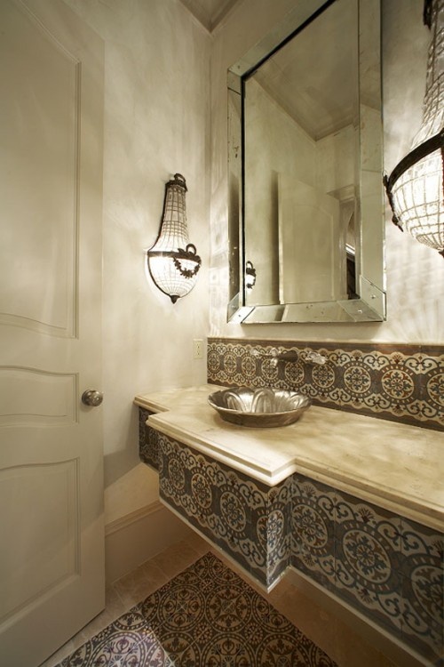 a neutral bathroom clad with Moroccan tiles on the floor and on the vanity plus chic lamps