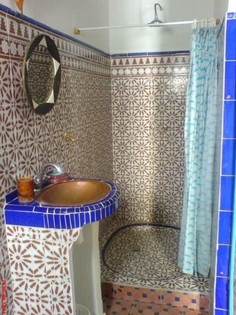 a Moroccan bathroom done with patterned tiles, touches of purple, a brass sink and an ornated mirror