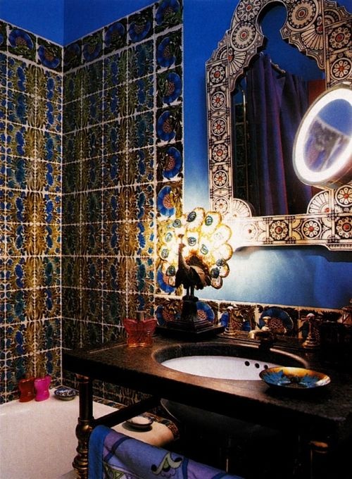 a colorful Moroccan bathroom with bright tiles, an ornated mirror, a cool peacock table lamp