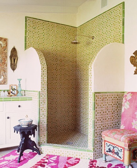 a Moroccan bathroom with green patterned tiles, wall lamps, a pink rug and chair