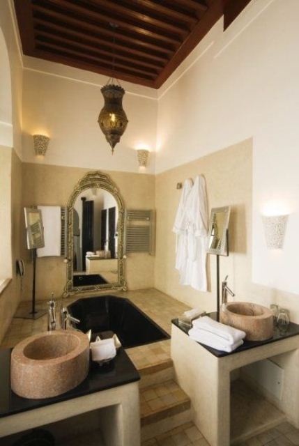 a neutral bathroom with Moroccan lanterns, stone sinks, a sunken bathtub, an ornated mirror 