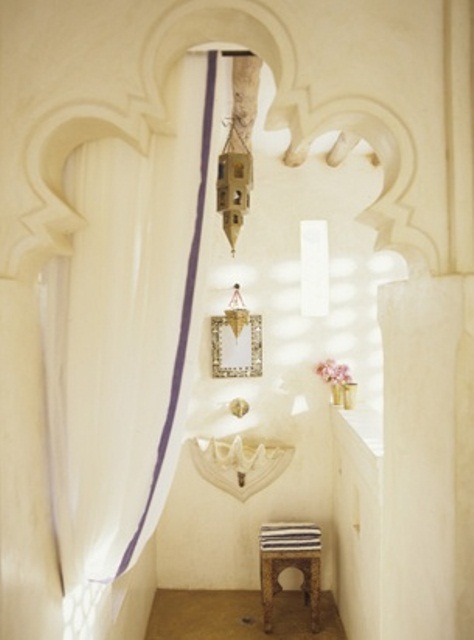 a neutral bathroom with a carved doorway, an embellished mirror, a seashell sink, a Moroccan lantern and a curtain