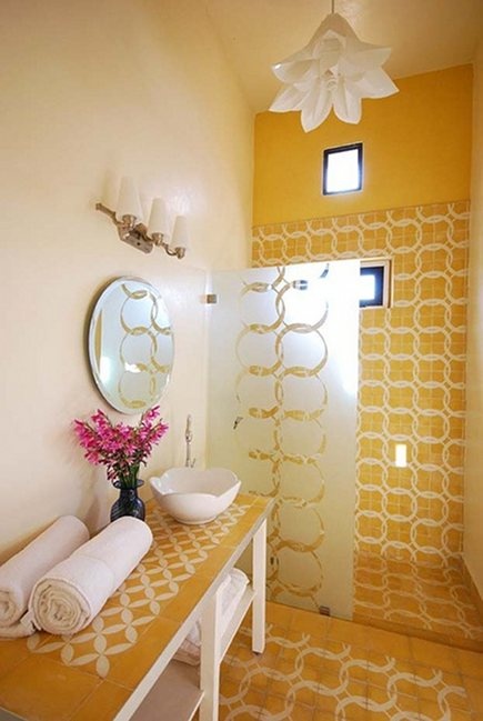 a bright yellow bathroom with catchy tiles, a bloom-shaped pendant lamp and a vanity clad with tiles