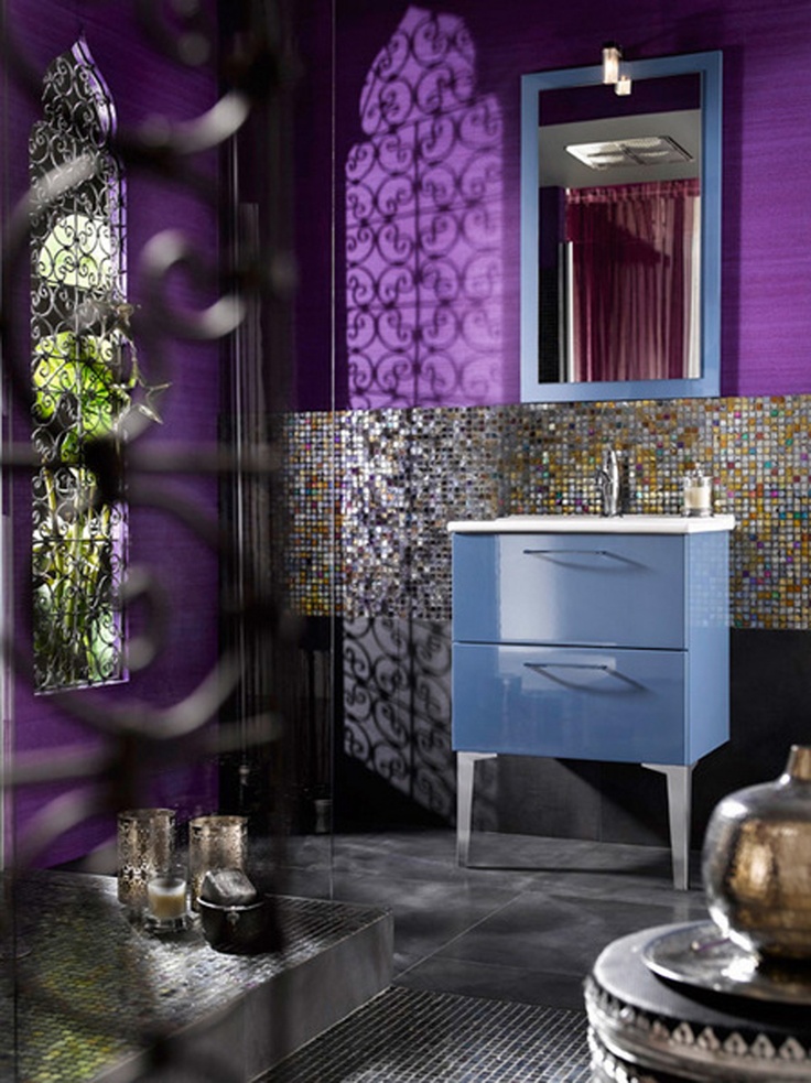 a super colorful Moroccan bathroom with purple walls, catchy tiles, a blue vanity and a blue framed mirror
