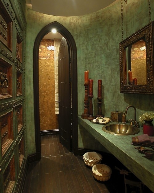 a green Moroccan bathroom with a brass sink, an ornated mirror, a wall with metal doors and pulls