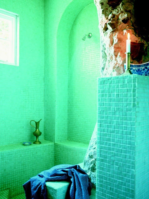 a bright turquoise and green bathroom with candles and a vintage metal jug