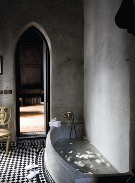 a Moroccan bathroom with concrete walls and a concrete tub, black and white tiles and an arched doorway