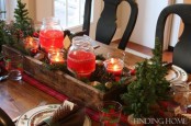 a rustic Christmas table setting with a plaid runner, mini Christmas trees, red candles in jars, pinecones and colorful napkins
