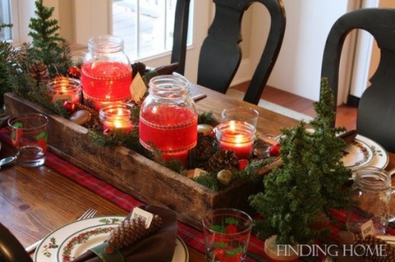 a rustic Christmas table setting with a plaid runner, mini Christmas trees, red candles in jars, pinecones and colorful napkins