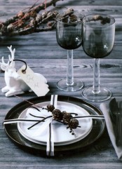 a Nordic rustic tablescape with an uncovered table, branches, a black placemat and plates plus grey glasses