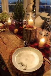 a cozy rustic table setting with an uncovered table, a red runner, tree stumps, candles in jars and a mini Christmas tree