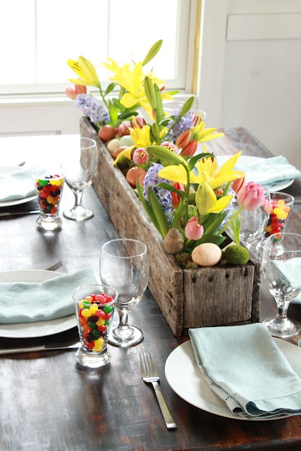 a colorful Easter centerpiece of a wooden box with grass, eggs and bright spring blooms is amazing for the tablescape