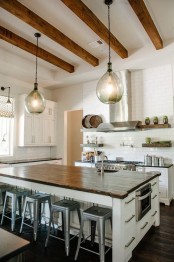 a white kitchen with chic farmhouse cabinetry, a large kitchen island, pendant lamps, rich-toned wooden beams that add coziness to the space