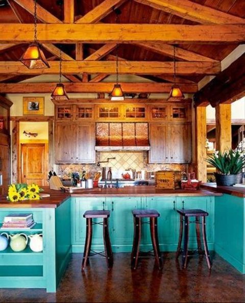 A bright kitchen with wooden upper cabinets and turquoise lower ones, rich toned wooden beams with pendant lamps for a more catchy and vintage look