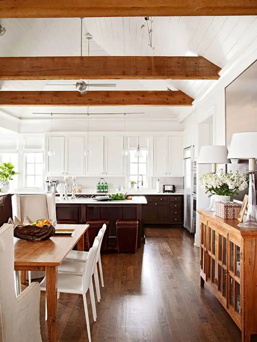 a modern two-tone farmhouse kitchen with upper white and lower dark cabinets, rich-tone wooden beams and pendant lamps that highlight the attic ceiling