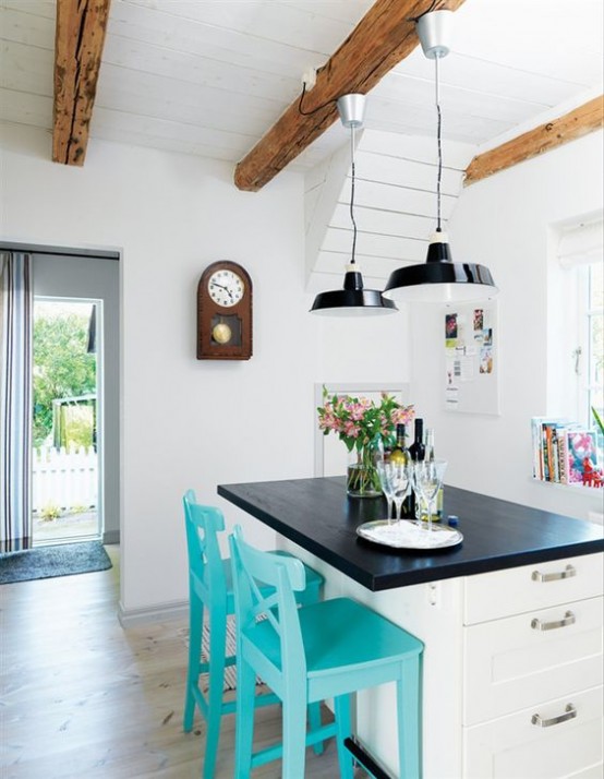 a white farmhouse kitchen with cozy white furniture, black pendant lamps and wooden beams that add interest and warm to the clean and airy space