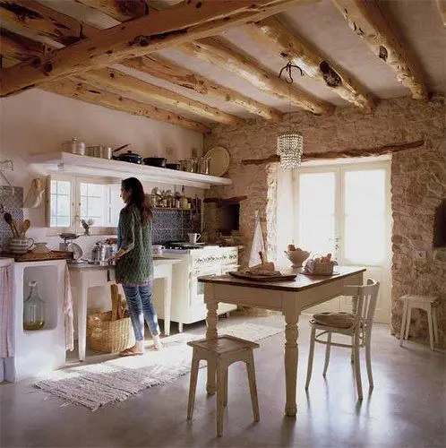 a French farmhouse kitchen with stone walls, exposed wooden beams and vintage white furniture and a crystal chandelier