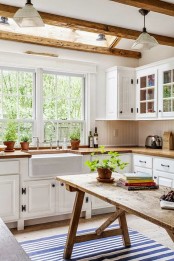 a white farmhouse kitchen with wooden countertops, a wooden table kitchen island and wooden beams that cozy up the kitchen