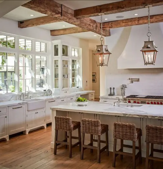 a neutral and refined kitchen with white cabinetry, wooden beams with elegant lamps and woven stools that add chic and coziness here
