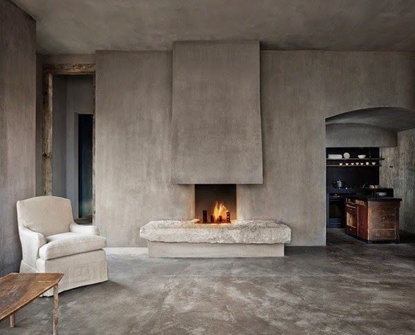 A wabi sabi living room with concrete walls and a fireplace, a matching floor and very few furniture pieces