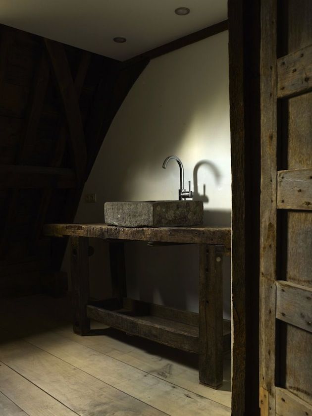 A wabi sabi bathroom with a wooden vanity, a stone sink and bare walls for a minimalist and rough look