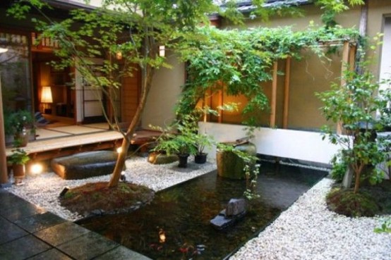a beautiful Japanese backyard with a stone covered space, a pond in the center and rocks and trees plus greenery
