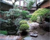 a calming Japanese garden with pebbles, large rocks, a wooden bridge, trees, lanterns and a pond
