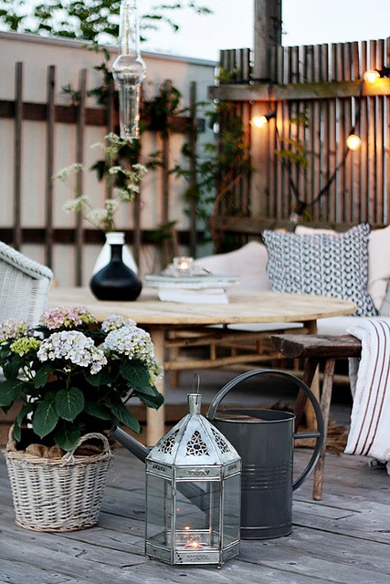 a rustic summer porch with simple rattan furniture, printed textiles and potted blooms and greenery