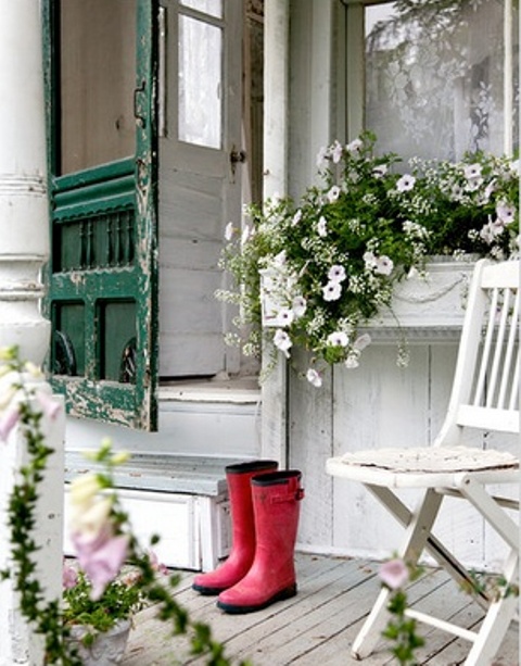 a white summer porch with shabby chic furniture and a door, rubber boots and potted flowers