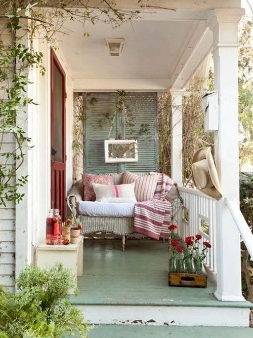 a small porch with a wicker loveseat, a bench, a crate and some colorful printed textiles