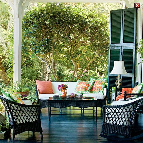 a lively summer porch done with dark wicker furniture, colorful printed pillows, a lamp and shutters