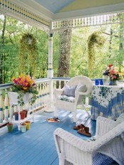 a bright blue summer porch with a blue floor, textiles, white furniture and potted blooms