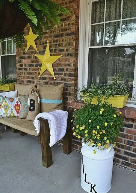 a rustic summer porch with a burlap covered bench, bright touches of yellow and potted flowers