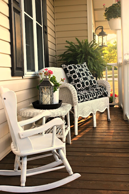 a small rustic porch with white wicker and wood furniture, candle lanterns and potted greenery