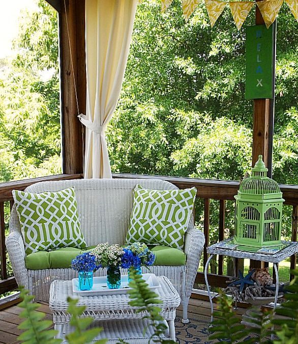 White wicker furniture, green printed textiles, grene signage and lanterns for a welcoming summer porch