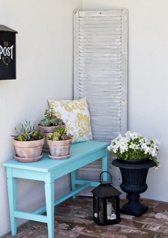 a beachy summer porch with a blue console, a whitewashed shutter, a candle lantern and potted succulents and blooms