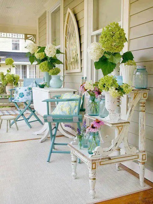 a shabby chic summer porch done with blue and neutral furniture and bright floral arrangements