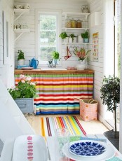 a bright kitchen with striped curtains, bold rugs, bright tableware and bold blooms and greenery